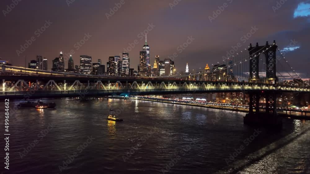 aerial rising above Manhattan Bridge East River view of two bridges from water and NYC skyline at night aerial rising above Manhattan Bridge East River view of two bridges from water and NYC skyline at night