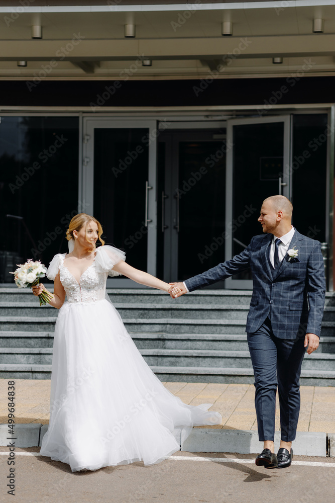 Happy bride and groom walking on the background of the hotel entrance