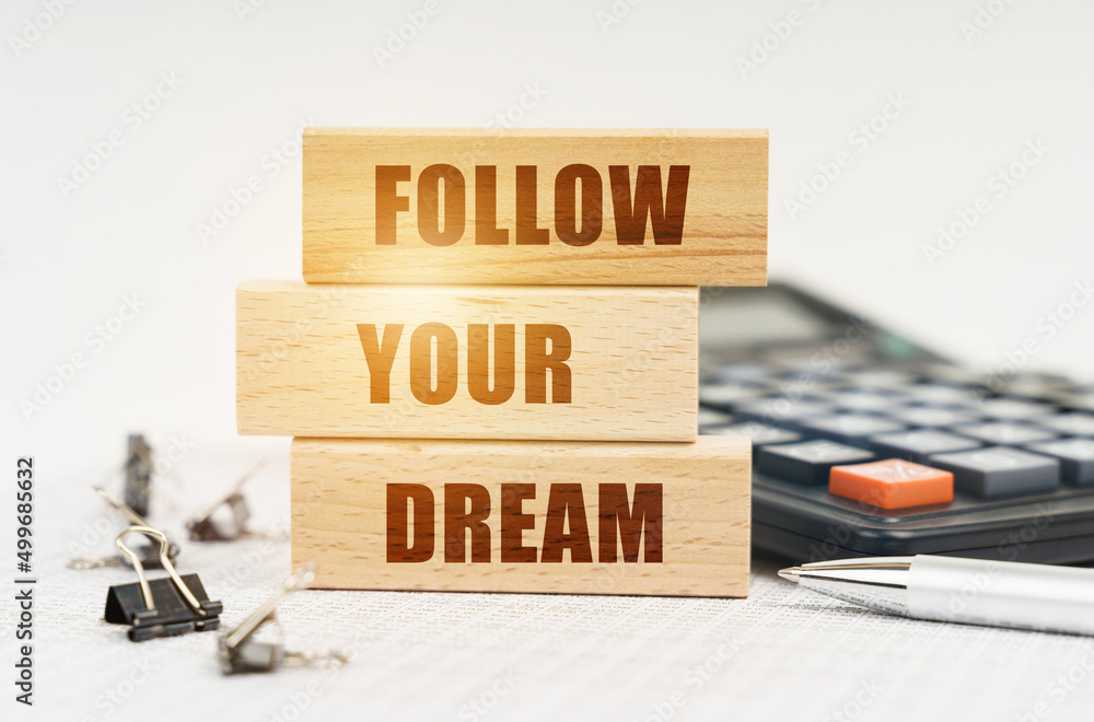 On the reports is a pen, calculator, clips and wooden boards with the inscription - FOLLOW YOUR DREAM On the reports is a pen, calculator, clips and wooden boards with the inscription - FOLLOW YOUR DREAM