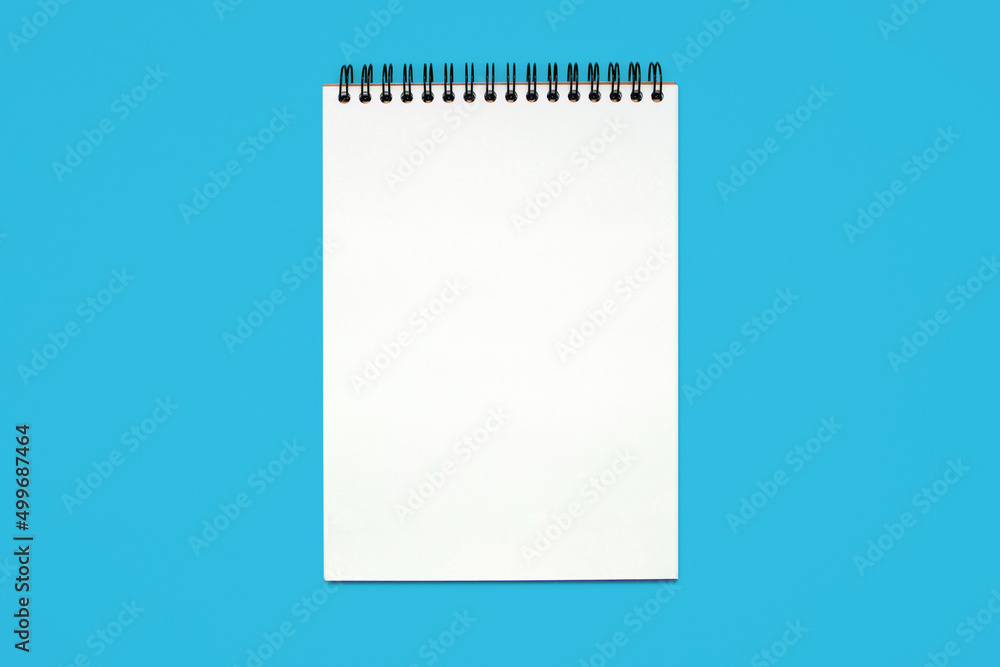 Notebook made of white paper with binding on a blue background. Blank notepad with free space for text. Notebook in classic binding without notes, top view Notebook made of white paper with binding on a blue background. Blank notepad with free space for text. Notebook in classic binding without notes, top view