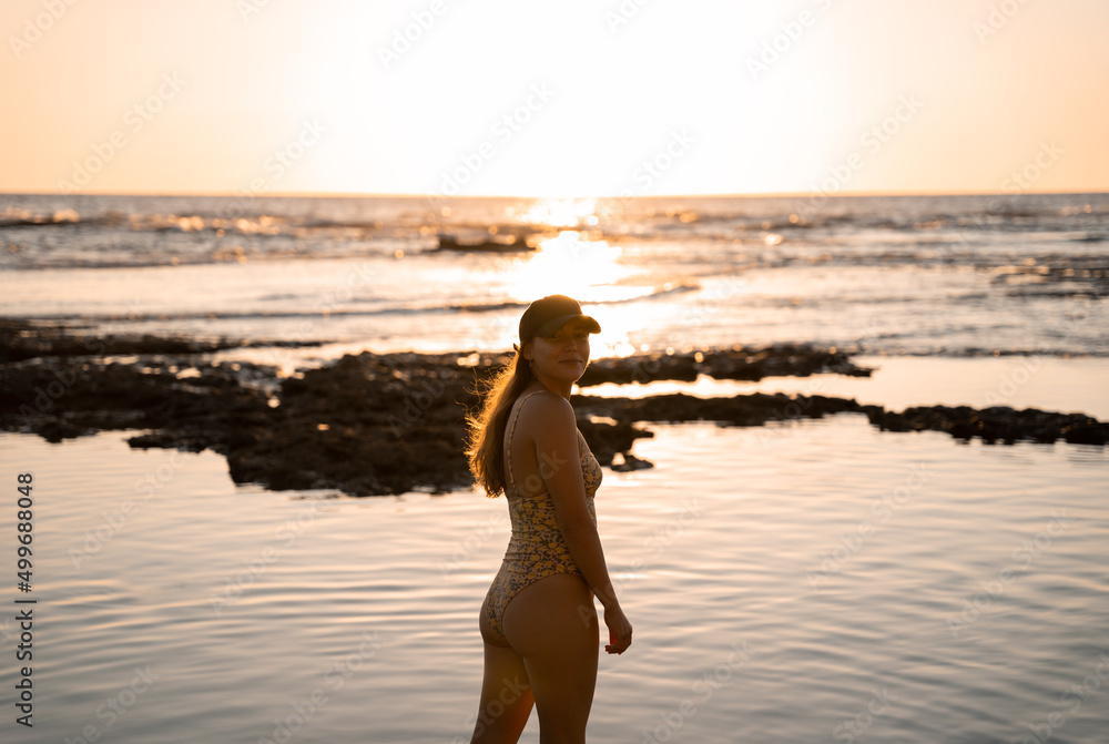 Young blonde woman is posing happily wwearing a cap on the beach during a summer sunset