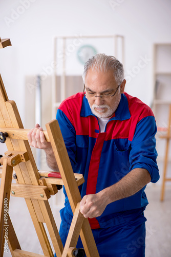 Old male carpenter repairing drawing easel