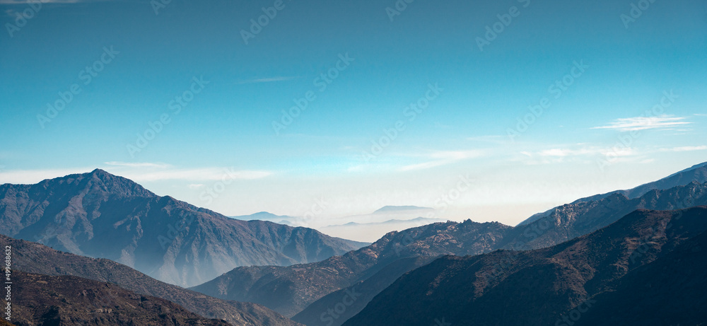 Horizontal panoramic view of mountain range in the distance getting lost in the fog in Cajon del Maipo, Chile.