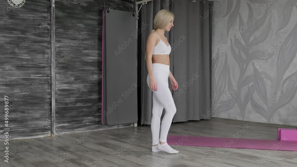 Sporty young woman stretching at home. Attractive fit woman stretching. Blonde female in white sportswear training indoors. 4K, UHD Sporty young woman stretching at home. Attractive fit woman stretching. Blonde female in white sportswear training indoors. 4K, UHD