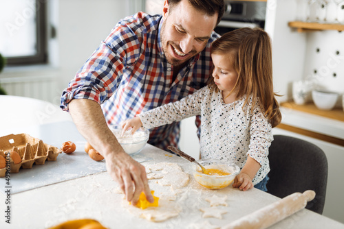 Cute small girl baking a cake with her father in the kitchen