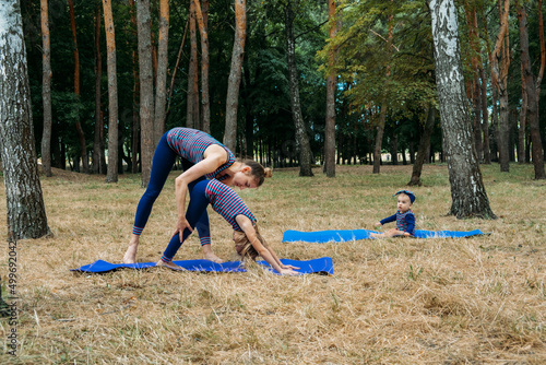 Family yoga. Mother and baby doing yoga Exercises for Beginners outdoors. Family doing yoga exercise in summer park