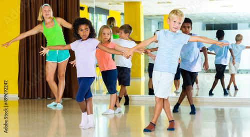Group of children practicing vigorous jive movements in dance class with female coach..