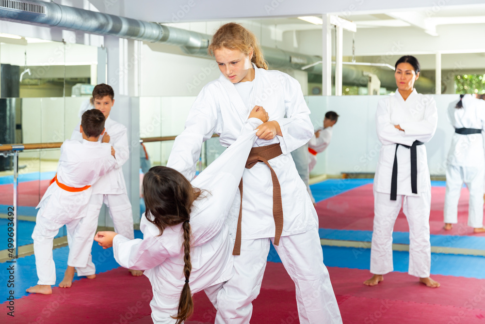 Fototapeta premium Focused school girls wearing white sports uniform practicing karate sparring in pair in gym