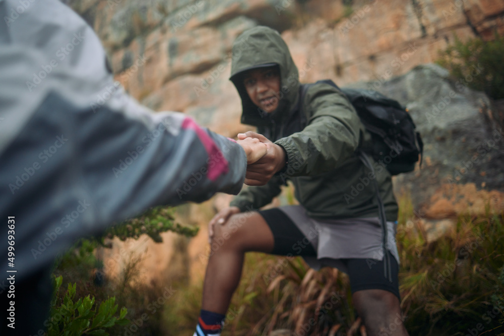 My hand will always be there when you reach out for help. Shot of a man helping his partner up a cliff while mountain climbing.