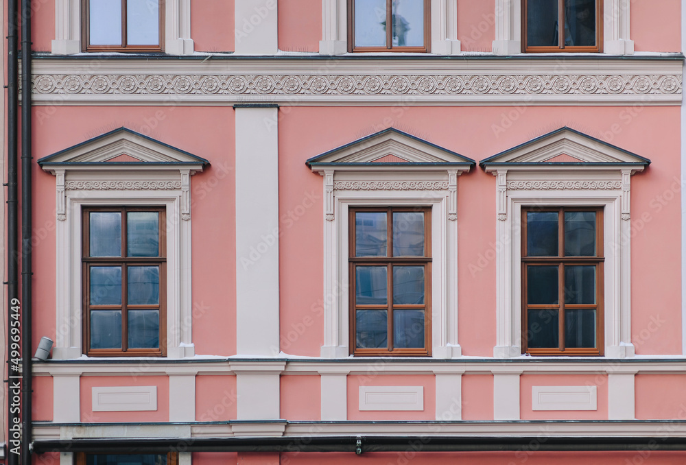 Obraz premium Windows on the facade of a pink house in the central historical part of the city. Beautiful decorative architecture with reliefs on white cornices and pilasters in Lviv, Ukraine.