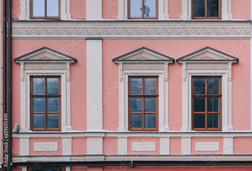 Windows on the facade of a pink house in the central historical part of the city. Beautiful decorative architecture with reliefs on white cornices and pilasters in Lviv, Ukraine.