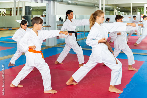 Group of kids training kata movements in gym with their female trainer.