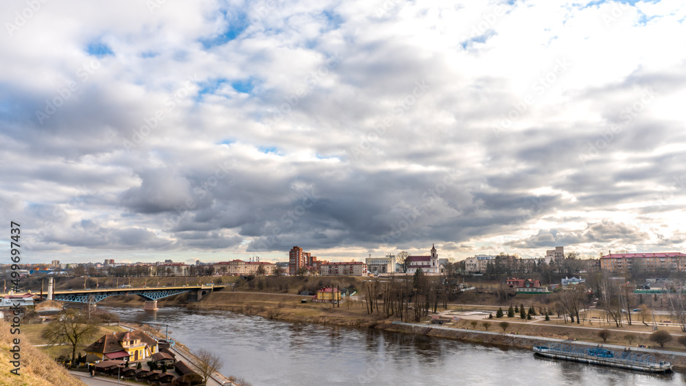 The movement of gray rain clouds over the river and a panorama of the city. View of the embankment along the river and the road bridge.