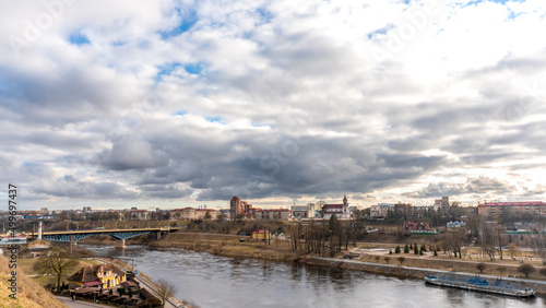 The movement of gray rain clouds over the river and a panorama of the city. View of the embankment along the river and the road bridge.