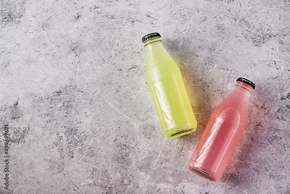 Bottles of refreshing fruit drinks, one yellow and one pink, laid on a stone surface. Bottles of refreshing fruit drinks, one yellow and one pink, laid on a stone surface.