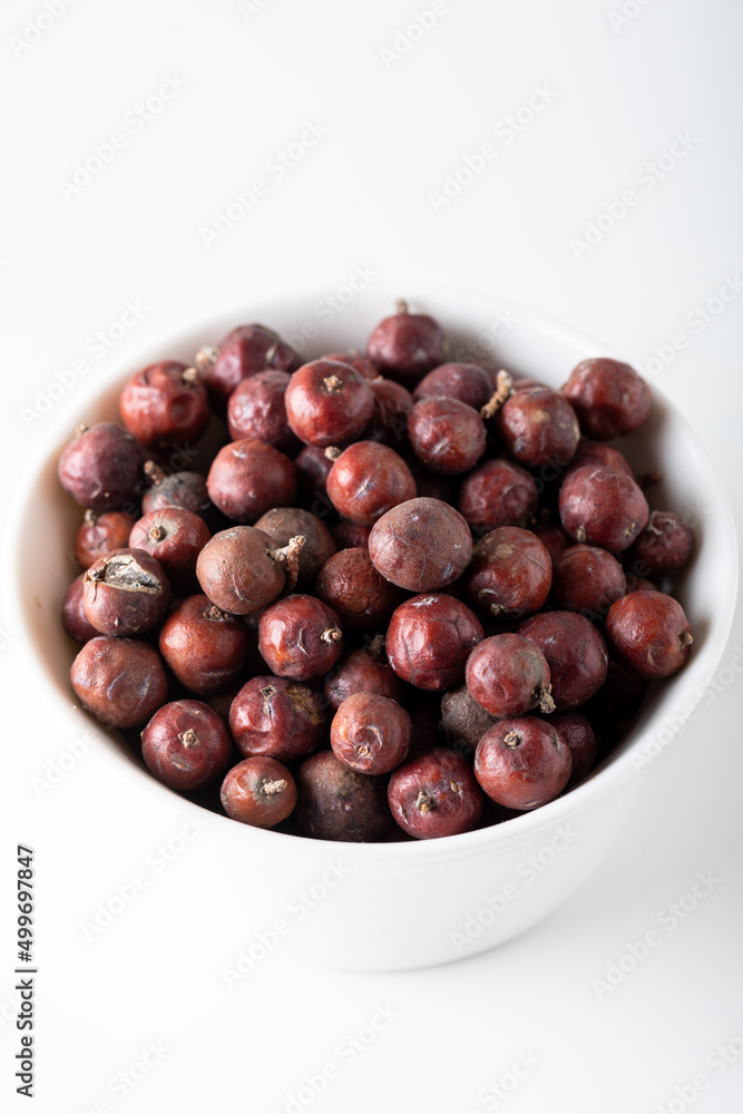 Obraz premium Juniper berries on white background. Juniper seeds in a white bowl isolated.