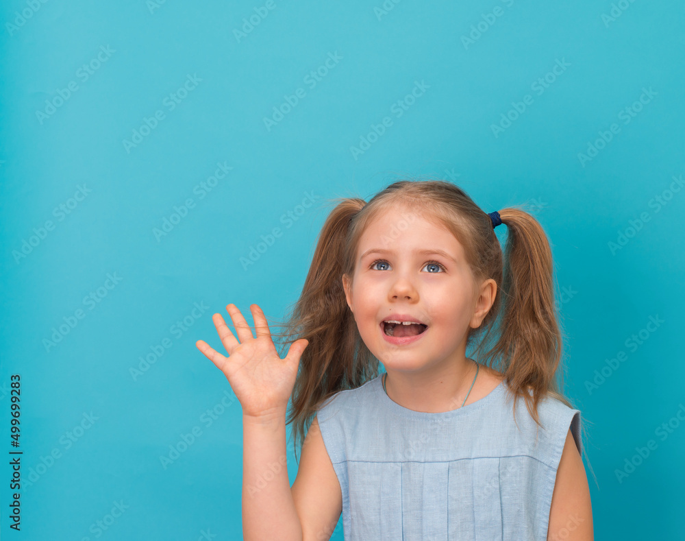 Little amazed girl looking up with copy-space on blue background. Children imagination and dream concept.