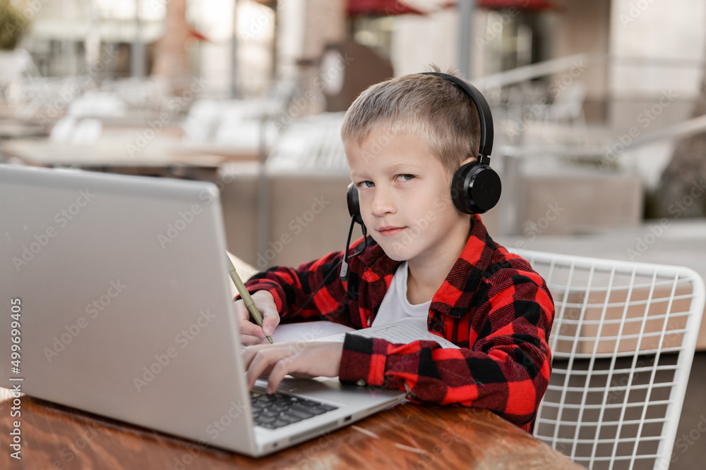 A schoolboy sits at a laptop in headphones and screams at the screen. A schoolboy sits at a laptop in headphones and screams at the screen.