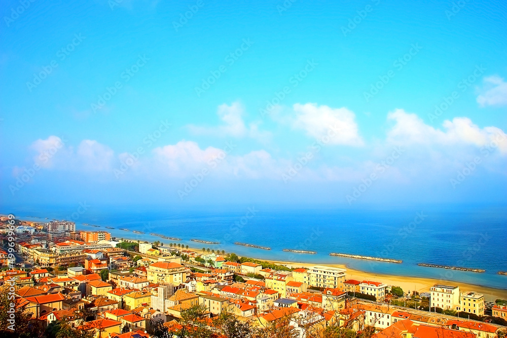 View from Cupra Alta (Marano) at an amazing coast of the Adriatic sea with the Italian town of Cupra Marittima lightened by the autumn sun under the blue sky with low white clouds