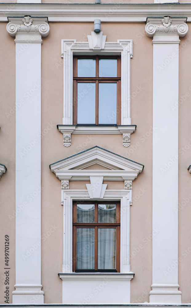 Two windows on the facade of a beige house in the central historical part of the city. Beautiful decorative architecture with reliefs on white cornices and pilasters in Lviv, Ukraine.