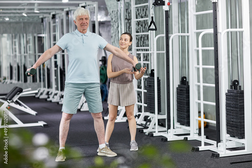 Full length portrait of senior man doing physical exercises in rehabilitation clinic with female therapist assisting