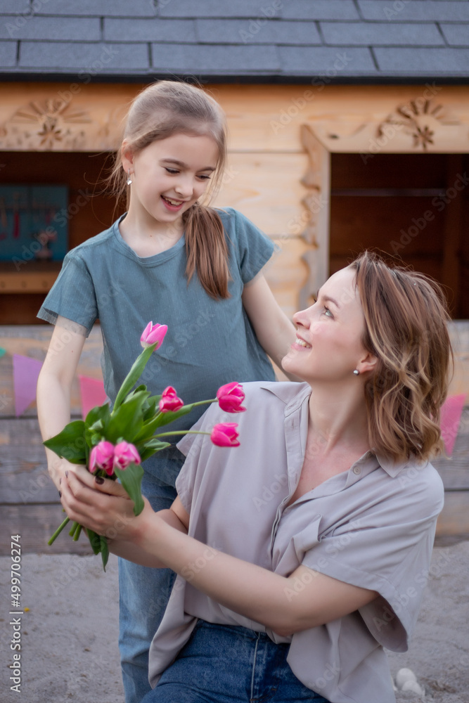 Happy mothers day. Child daughter is congratulating mom and giving her flowers tulips. Mum and girl smiling and hugging. Family holiday and togetherness Happy mothers day. Child daughter is congratulating mom and giving her flowers tulips. Mum and girl smiling and hugging. Family holiday and togetherness