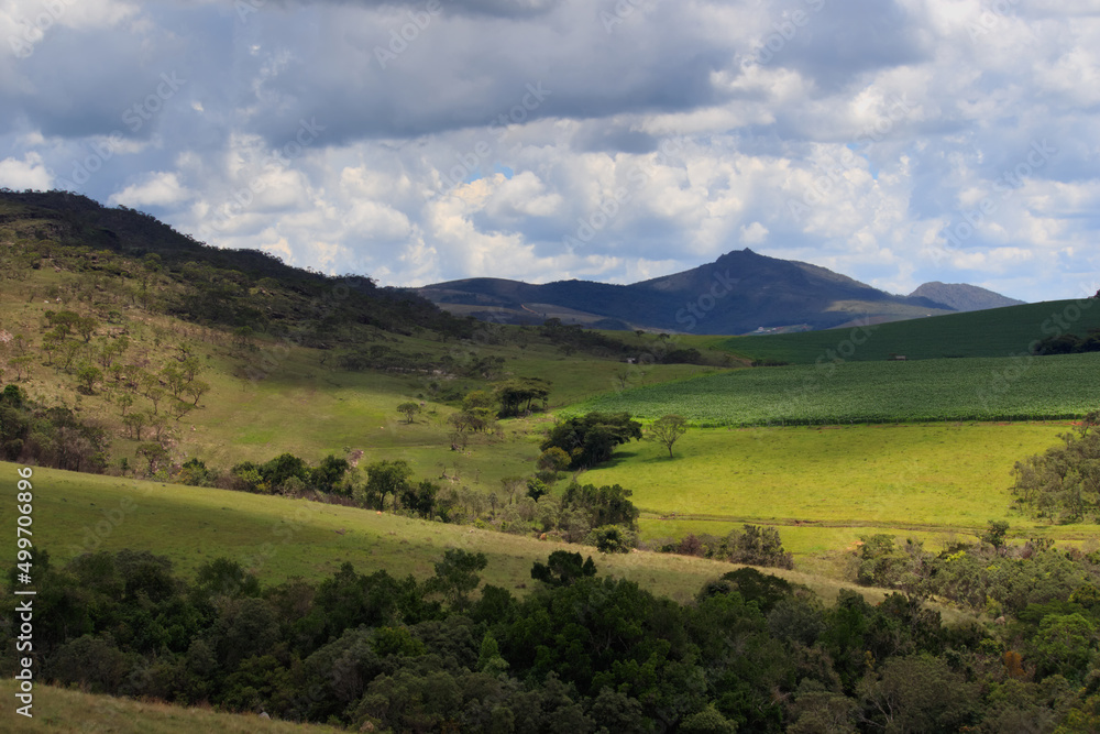 view of a green valley with the silhouette of the Gaviao peak in the background, under a sky with thick clouds that create shadows in the valley.