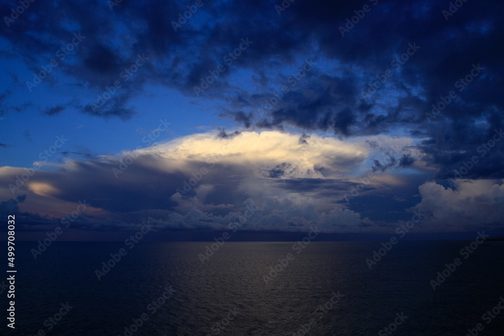 Panoramic view of ocean waters horizon line with dramatic cumulus thunderstorm cloudscape in blue sky background. Panoramic view of ocean waters horizon line with dramatic cumulus thunderstorm cloudscape in blue sky background.