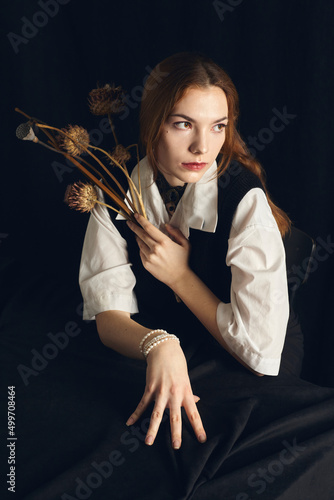 portrait of a pensive, stylish woman on a black background with dried flowers and a pearl bracelet