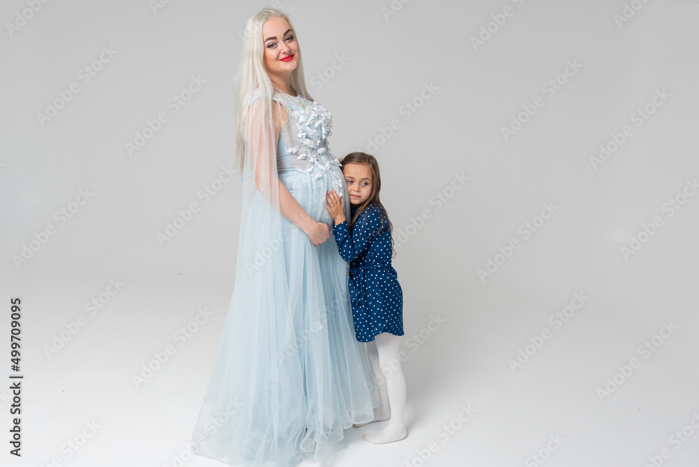 Beautiful, young pregnant woman and her little daughter, on a light background. Happy family concept