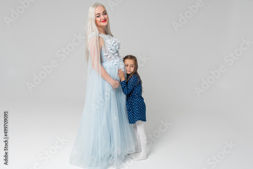 Beautiful  young pregnant woman and her little daughter  on a light background. Happy family concept