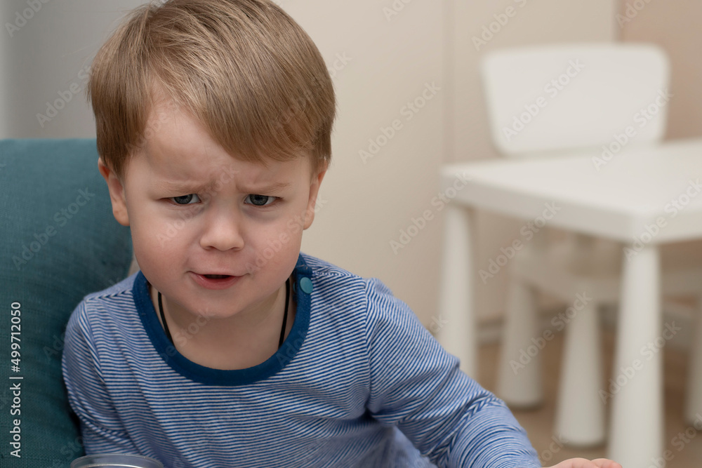 A small Caucasian handsome boy emotionally frowns his eyebrows in a home interior in a striped sweater. Close-up A small Caucasian handsome boy emotionally frowns his eyebrows in a home interior in a striped sweater. Close-up