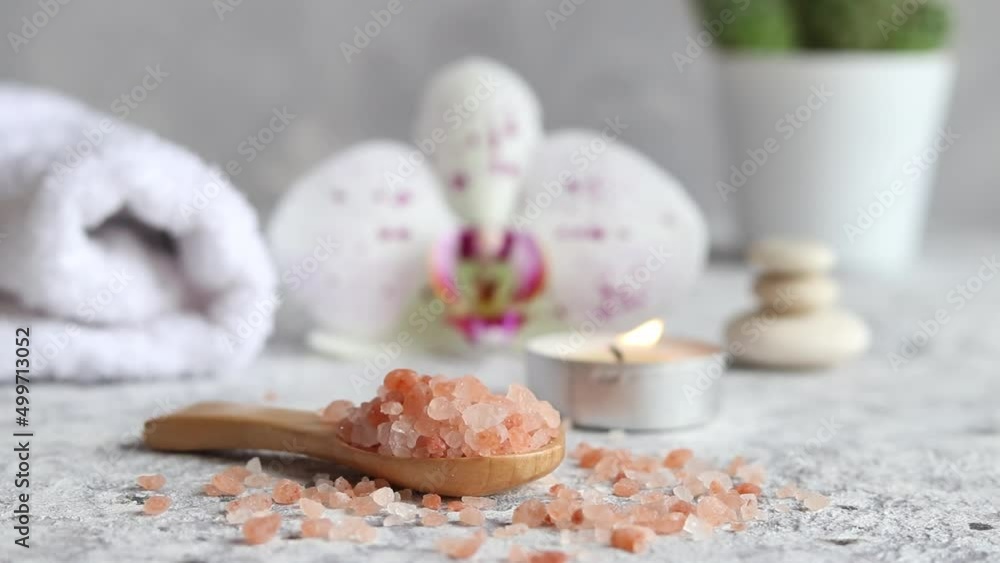 Pink himalayan salt close-up on a wooden spoon with candle, orchid flower and towel. Beauty and spa concept. Selective focus Pink himalayan salt close-up on a wooden spoon with candle, orchid flower and towel. Beauty and spa concept. Selective focus