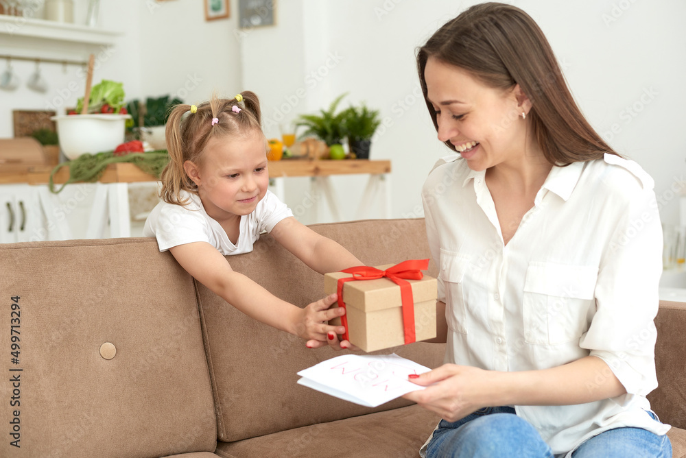 Lovely little girl gives her mom a card and a gift for March 8 or mother's day. Loving family concept. Lovely little girl gives her mom a card and a gift for March 8 or mother's day. Loving family concept.