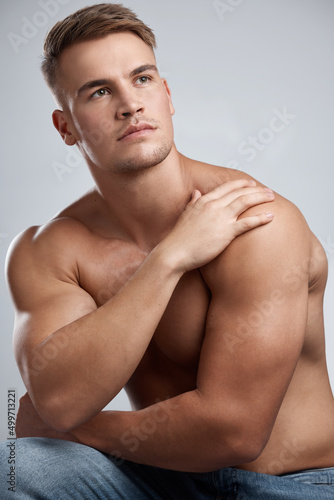 Sculpted like a king. Studio shot of a muscular young man looking thoughtful while posing against a grey background.