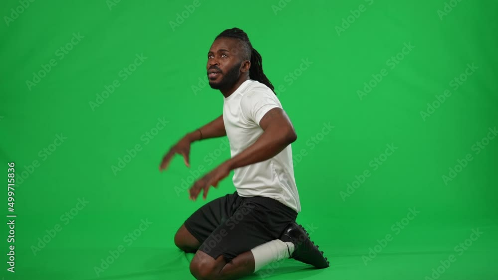 Wide shot excited African American footballer rejoicing goal on green screen. Satisfied smiling happy sportsman sitting on knees gesturing success at chromakey background mockup Wide shot excited African American footballer rejoicing goal on green screen. Satisfied smiling happy sportsman sitting on knees gesturing success at chromakey background mockup