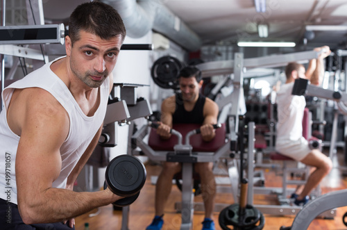 Concentrated sporty guy during workout in gym with dumbbells