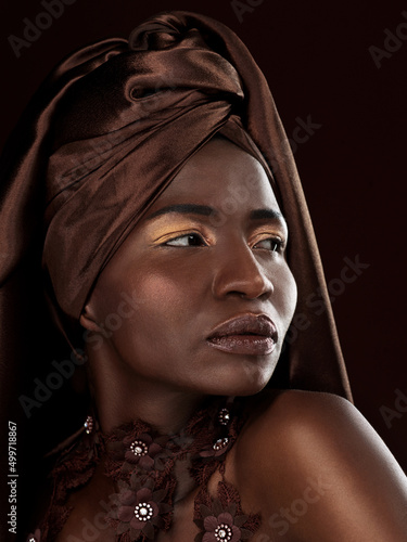 Rocking her head wrap. Studio shot of an attractive young woman posing in traditional African attire against a black background.