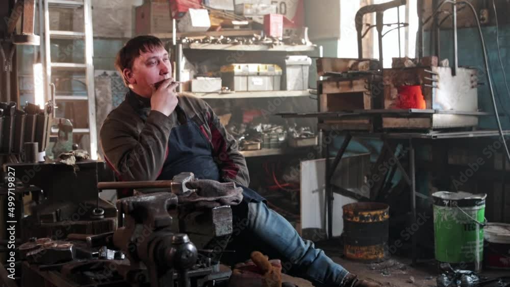 A man sitting in blacksmith workshop and smoking a cigarette A man sitting in blacksmith workshop and smoking a cigarette