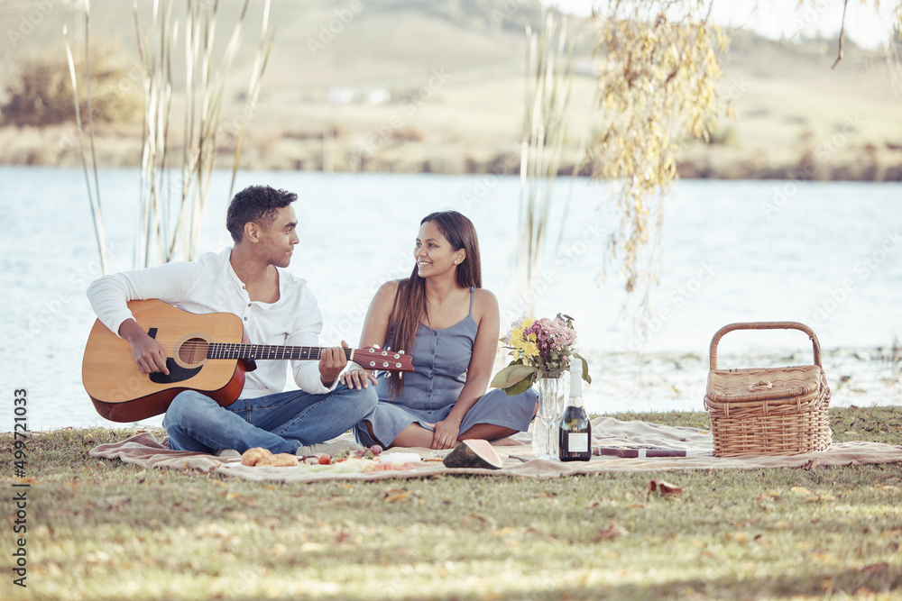 I wrote a song for you. Full length shot of a young woman sitting with her boyfriend while he plays the guitar during their picnic date.