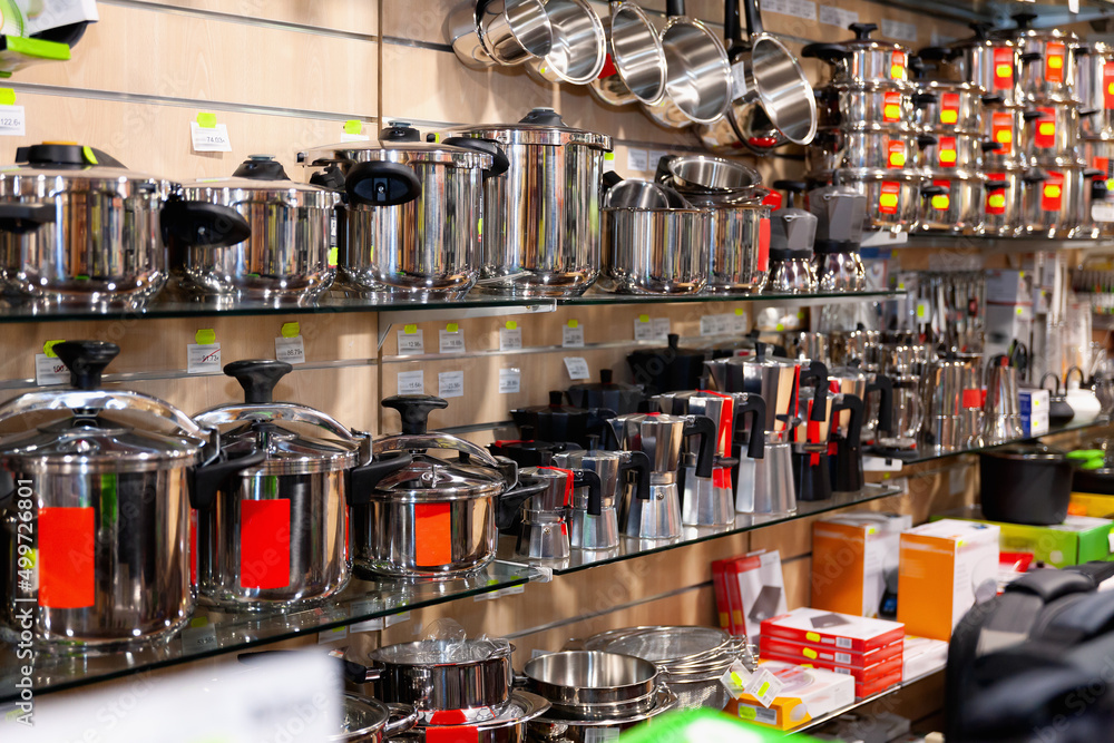 Shelves with stainless steel pots, saucepans, pressure cookers, coffee makers at kitchen utensils store