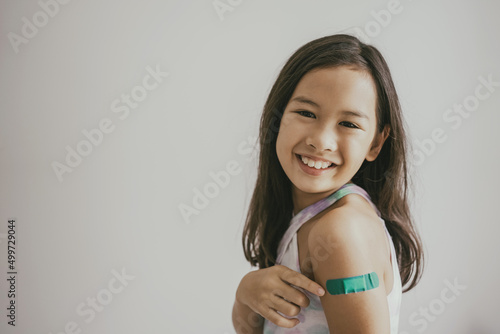 Foto Mixed Asian preteen girl showing her arm with bandage after got vaccinated or in