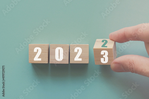 Hand flipping over wooden block of 2022 to 2023, New Year Resolutions, business concept