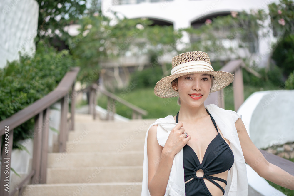 Woman in black dress and straw hat walking on tropical garden resort.