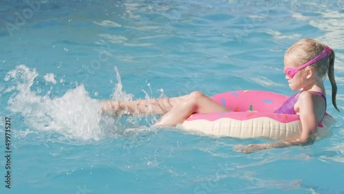 girl in swimming pool, child having fun, sitting on pink donut swimming ring, playing under water. Summer travel family hotel vacation tourists photo