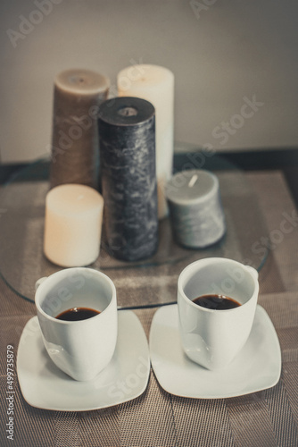 Two white cups of hot aromatic coffee on a brown table with candles. Composition in brown and beige tones.