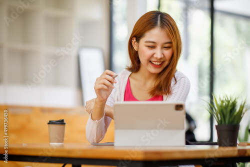 Fotografie Portrait of a beautiful young and intelligent-looking Japanese Asian woman student wearing a white shirt and pink tracker smiling as she works on her laptop in a university classroom