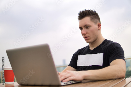 Young professional businessman wearing casual clothes and using modern laptop outdoors in a cafeteria.