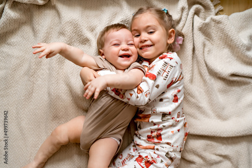 Obraz na plátně cheerful sister and younger brother hugging each other and lying on a blanket, l
