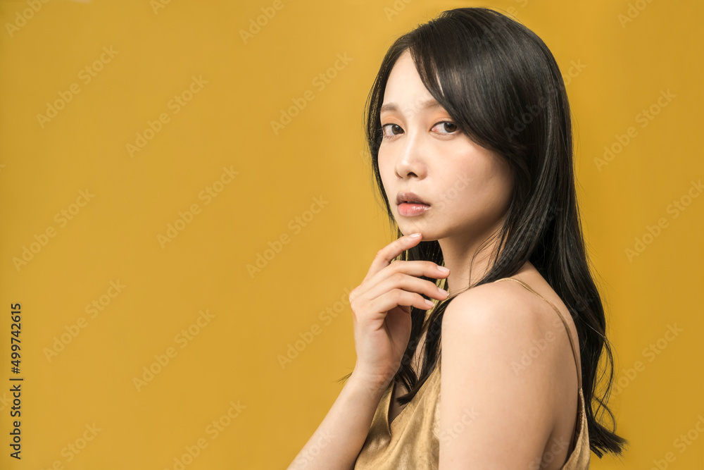 金色の背景の前に立つ黒髪の女性